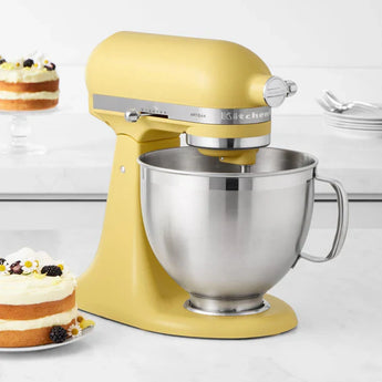 Crate & Barrel yellow stand mixer with stainless steel bowl on kitchen counter, next to layered cakes – electrics up to 10% off