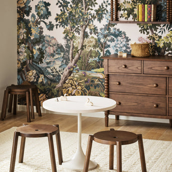 Round white dining table with wooden stools on a neutral rug, styled in a cozy dining space with botanical wallpaper.