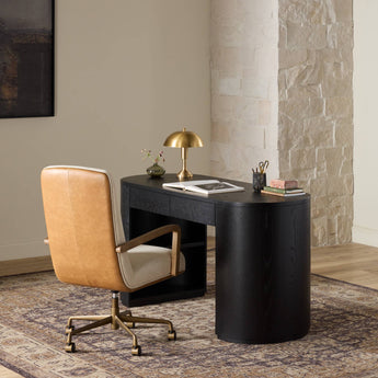 Modern home office setup with a black wood desk, upholstered swivel chair, table lamp, and patterned area rug.